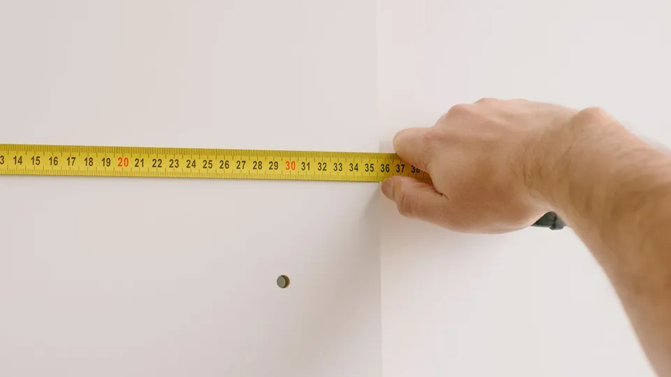 壁の隅でメジャーを使って幅を測っている様子