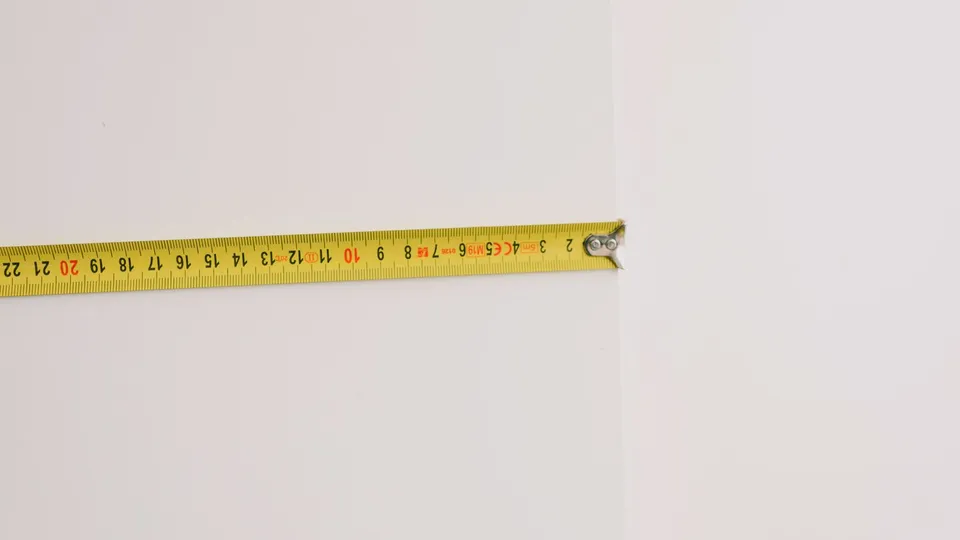 壁際でメジャーを使って隙間の幅を測っている様子